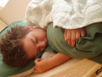 Mörkhårig pojke ligger på sidan och sover i en säng med grönt täcke och kudde
